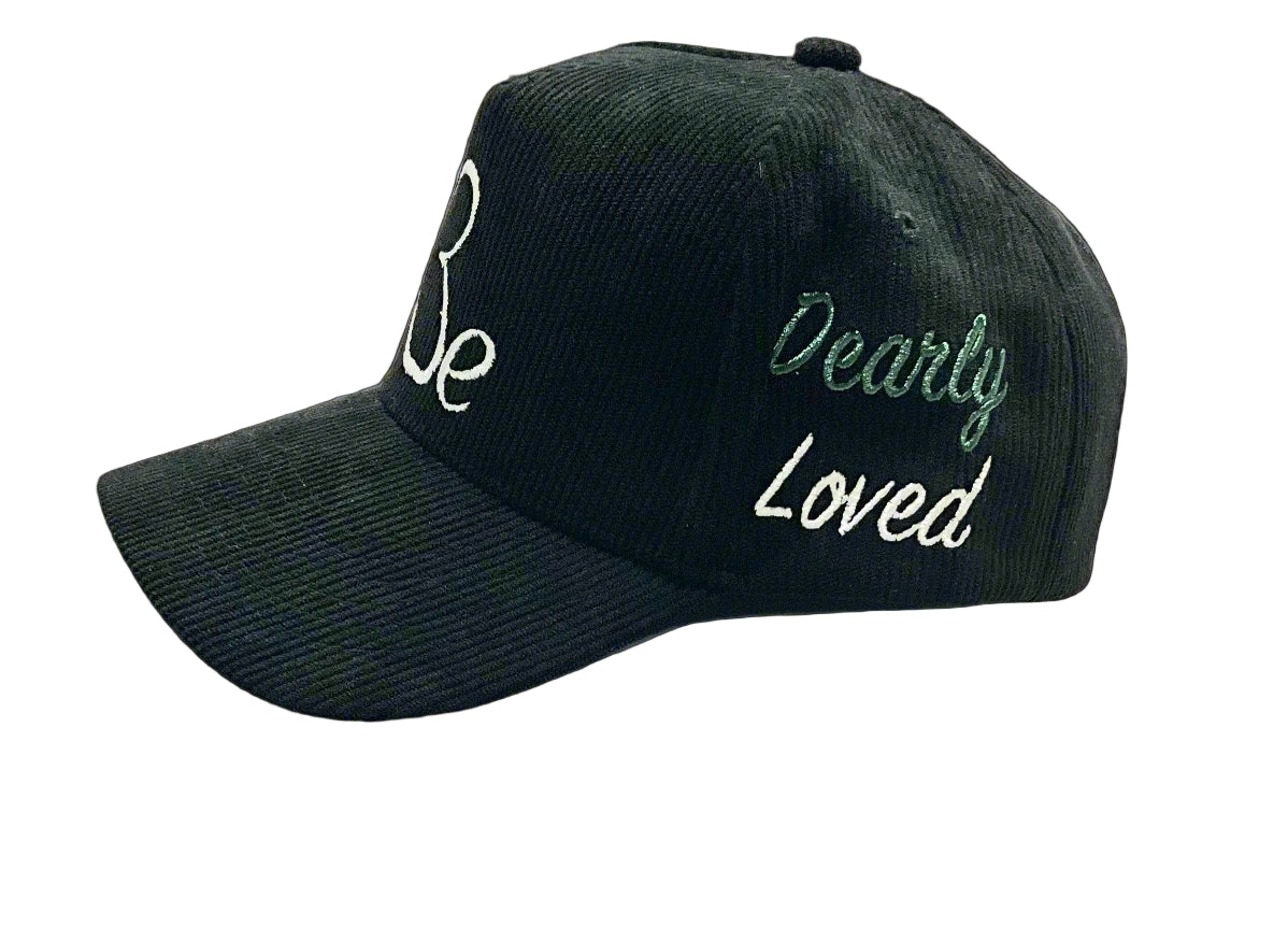 A black cap with the text 'Be' and 'Dearly Loved' embroidered on it, displayed in various angles and a sketch showing the design process.